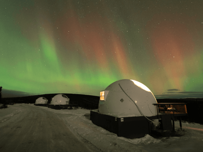 Aurora borealis glimmering behind several Borealis Basecamp igloos